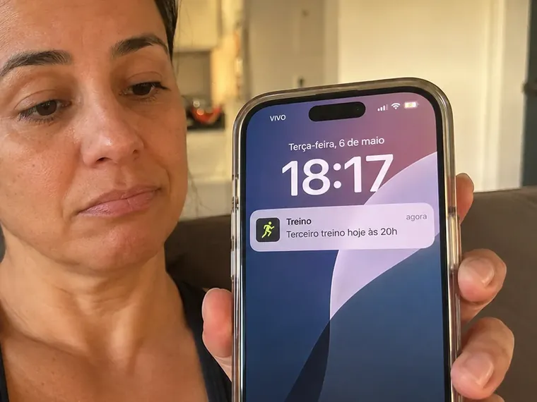 Mulher no sofá olhando a tela do celular com um lembrete de treino que já foi adiado